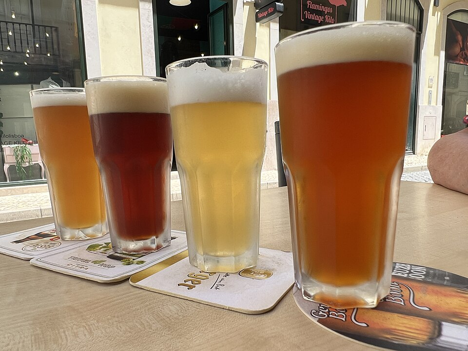 A flight of four beers of varying color in tall glasses on an outdoor café table in Lisbon
